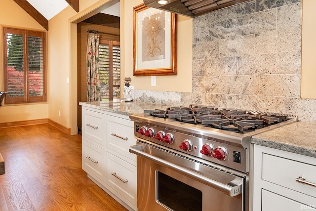 kitchen featuring white cabinetry, stainless steel range, light stone counters, lofted ceiling, and light wood-type flooring