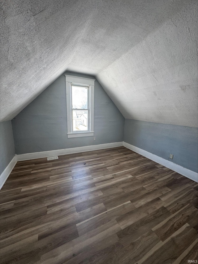 additional living space featuring lofted ceiling, a textured ceiling, and dark wood-type flooring