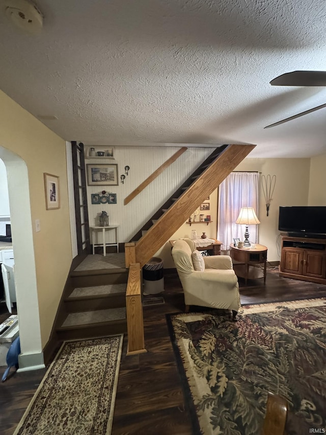 living room with a textured ceiling, ceiling fan, and dark hardwood / wood-style floors