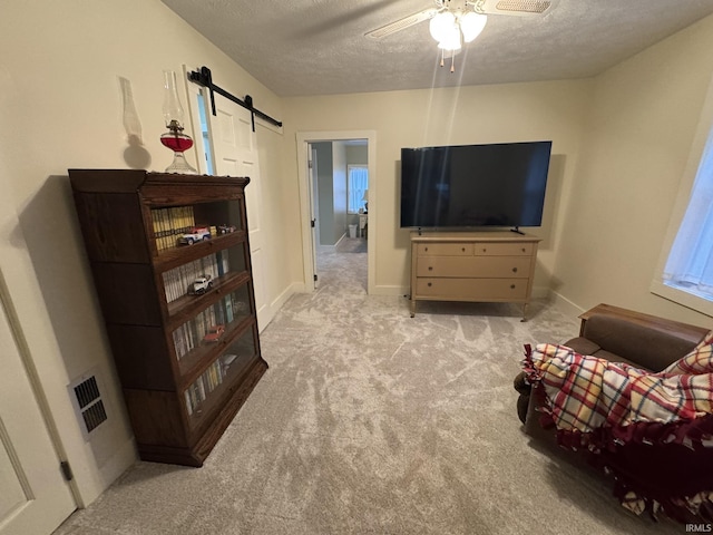 carpeted living room featuring ceiling fan, a barn door, and a textured ceiling