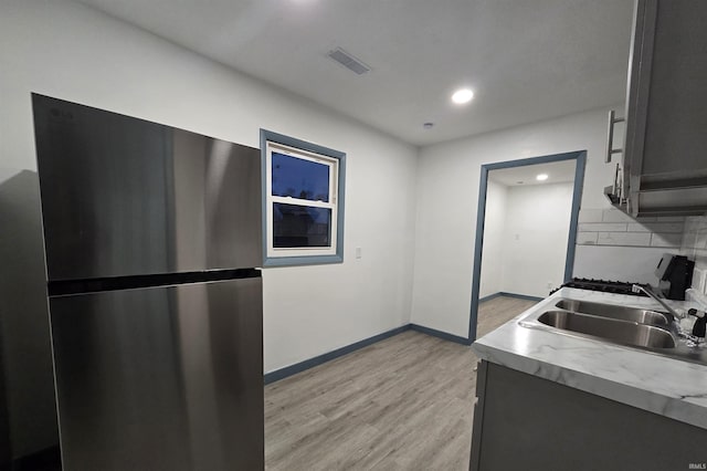 kitchen with backsplash, stainless steel fridge, sink, and light wood-type flooring