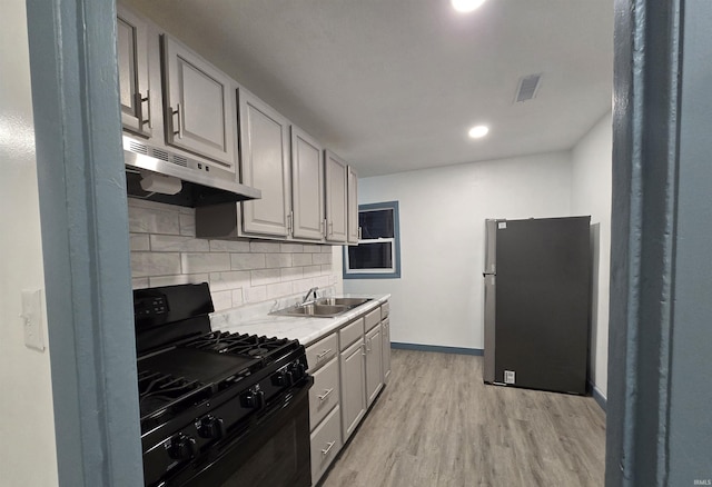 kitchen featuring gas stove, stainless steel refrigerator, sink, gray cabinets, and light wood-type flooring