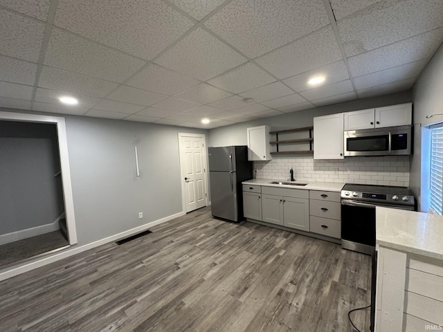 kitchen featuring sink, stainless steel appliances, hardwood / wood-style floors, a paneled ceiling, and decorative backsplash