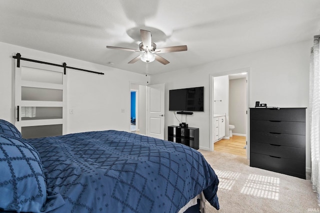 carpeted bedroom featuring a barn door, ceiling fan, and connected bathroom