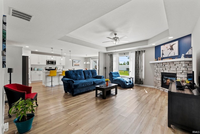 living room featuring a tray ceiling, ceiling fan, a fireplace, and light hardwood / wood-style floors