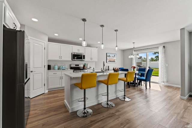 kitchen featuring hanging light fixtures, light hardwood / wood-style flooring, an island with sink, white cabinetry, and stainless steel appliances