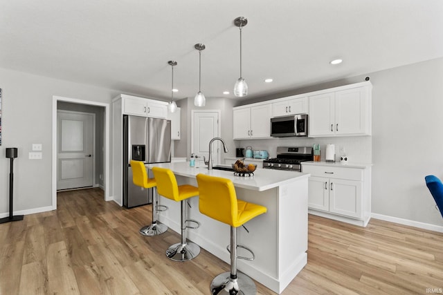 kitchen with a breakfast bar, a center island with sink, white cabinets, light wood-type flooring, and stainless steel appliances