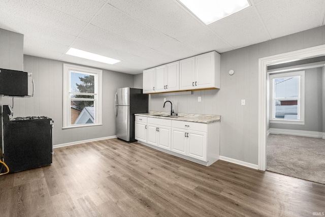 kitchen with a wealth of natural light, wood-type flooring, white cabinetry, sink, and stainless steel refrigerator