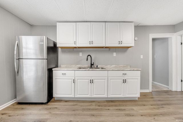 kitchen featuring light wood-type flooring, sink, stainless steel refrigerator, and white cabinetry