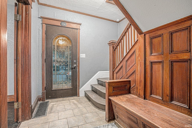 foyer entrance featuring light tile patterned flooring, crown molding, and a textured ceiling