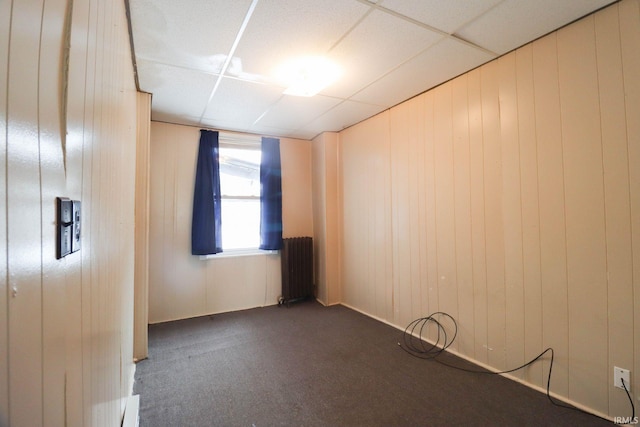 carpeted spare room with radiator, a drop ceiling, and wooden walls