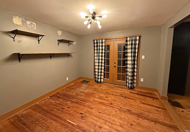 spare room featuring hardwood / wood-style floors, an inviting chandelier, and french doors