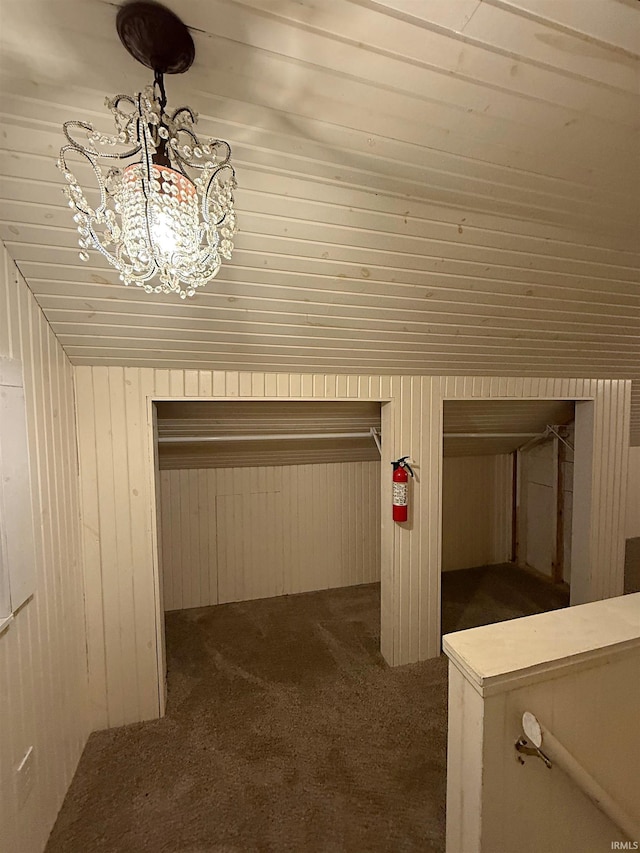 interior space with dark colored carpet, a notable chandelier, wood walls, and lofted ceiling