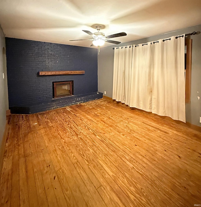 empty room featuring wood-type flooring, a brick fireplace, and ceiling fan