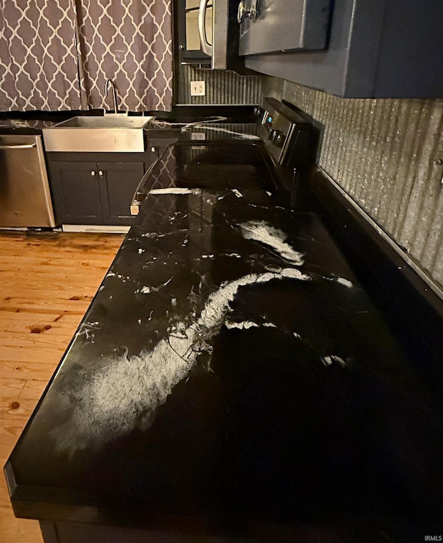 interior space featuring dark stone counters, black range with electric cooktop, sink, dishwasher, and light hardwood / wood-style floors