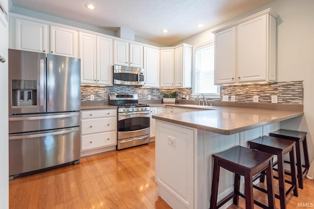 kitchen featuring white cabinets, sink, appliances with stainless steel finishes, light hardwood / wood-style floors, and kitchen peninsula