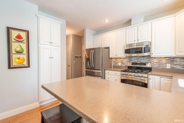 kitchen featuring light wood-type flooring, appliances with stainless steel finishes, tasteful backsplash, white cabinetry, and a breakfast bar area