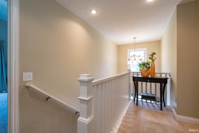 hallway featuring a chandelier, a textured ceiling, and light colored carpet