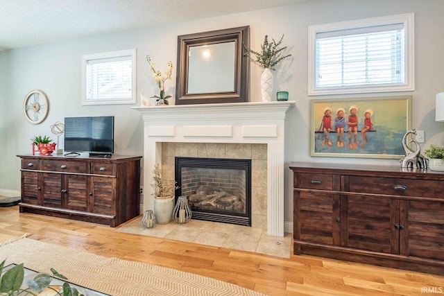 living area with a tile fireplace, a wealth of natural light, and hardwood / wood-style floors