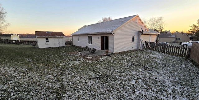 back house at dusk featuring a lawn and a storage shed