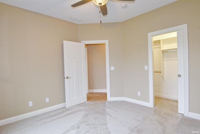 unfurnished bedroom featuring a spacious closet, a closet, ceiling fan, and light colored carpet