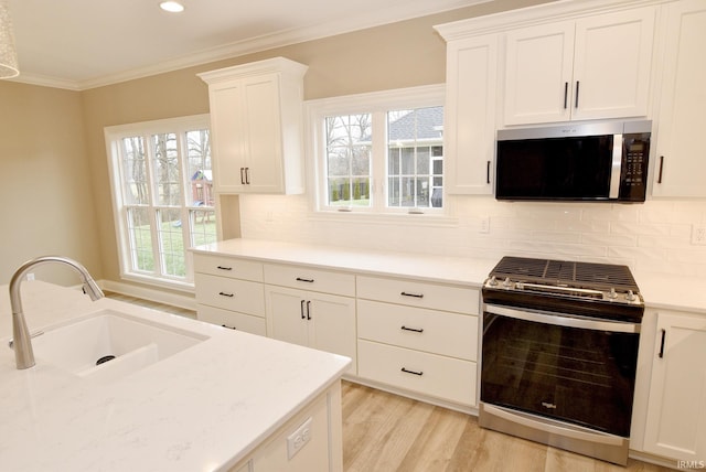 kitchen featuring backsplash, a healthy amount of sunlight, sink, stainless steel range oven, and white cabinetry