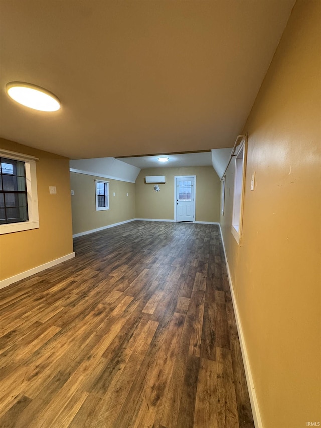 unfurnished living room with dark wood-type flooring, vaulted ceiling, and a wall unit AC