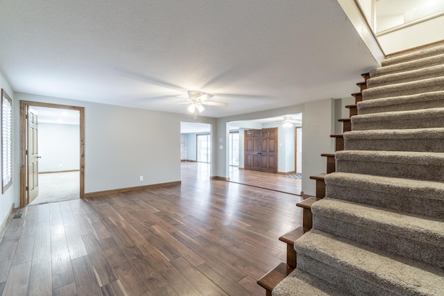 unfurnished living room featuring a textured ceiling, ceiling fan, and dark wood-type flooring