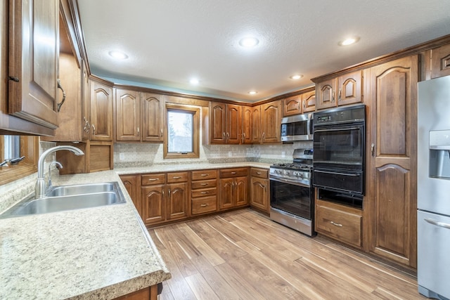 kitchen with decorative backsplash, appliances with stainless steel finishes, light wood-type flooring, a textured ceiling, and sink