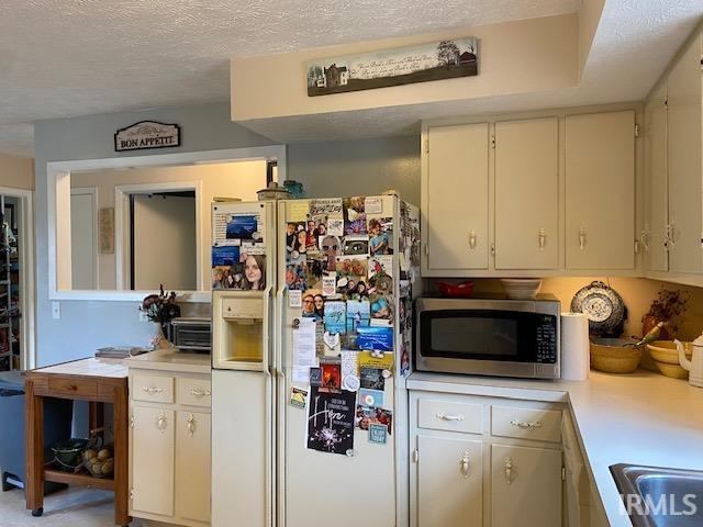 kitchen featuring sink, white refrigerator with ice dispenser, and a textured ceiling