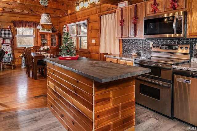 kitchen featuring stainless steel appliances, backsplash, wooden walls, a kitchen island, and light wood-type flooring