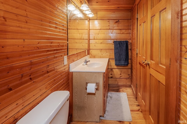 bathroom featuring hardwood / wood-style floors, vanity, wood walls, and toilet