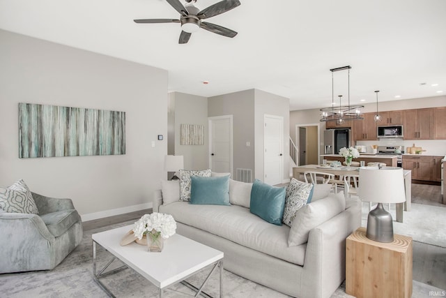 living room with ceiling fan with notable chandelier and light hardwood / wood-style flooring