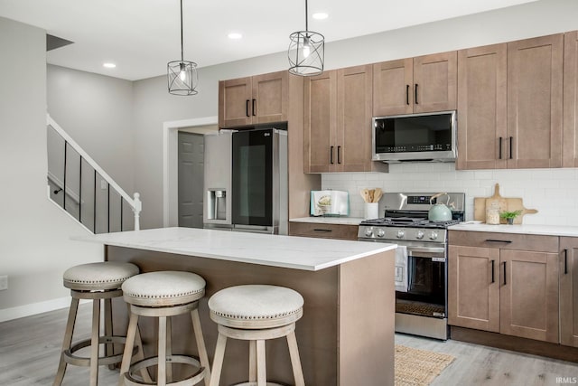 kitchen with a kitchen bar, appliances with stainless steel finishes, pendant lighting, light hardwood / wood-style floors, and a kitchen island