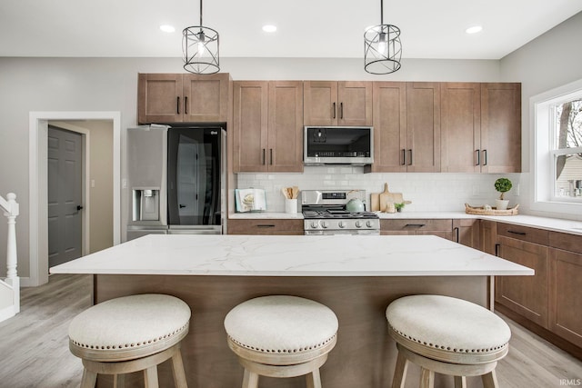 kitchen with decorative light fixtures, appliances with stainless steel finishes, and light hardwood / wood-style flooring