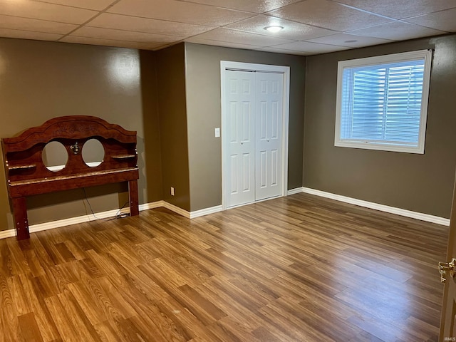 unfurnished bedroom with a paneled ceiling, a closet, and hardwood / wood-style flooring