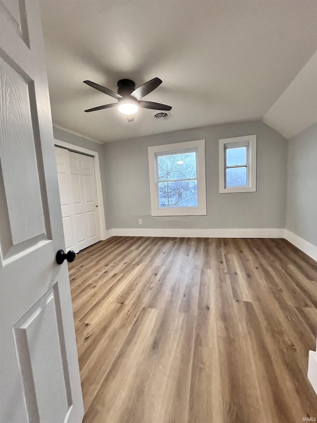 unfurnished bedroom featuring ceiling fan, vaulted ceiling, a closet, and light hardwood / wood-style flooring