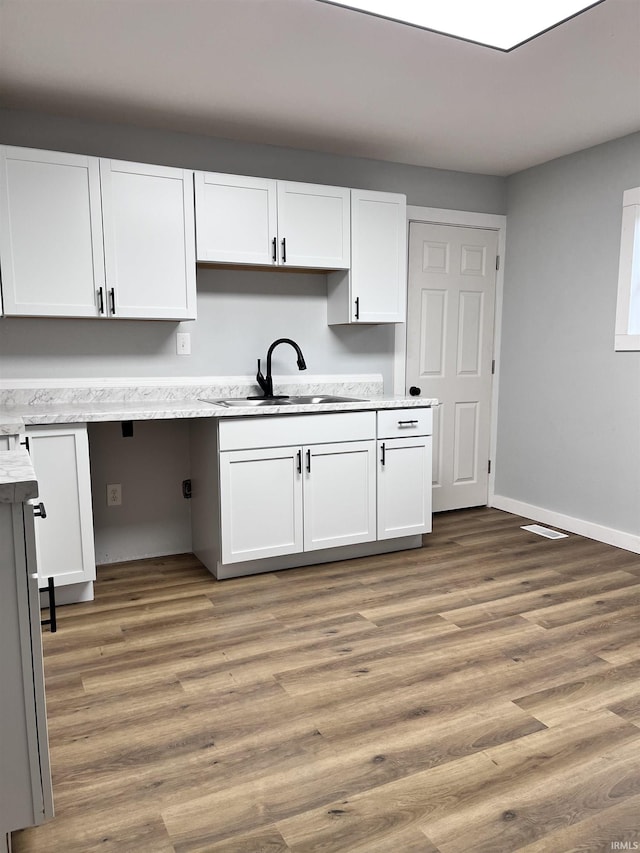 kitchen with wood-type flooring, white cabinetry, and sink