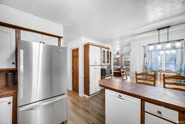 kitchen featuring dishwasher, white cabinetry, stainless steel fridge, hanging light fixtures, and light hardwood / wood-style floors