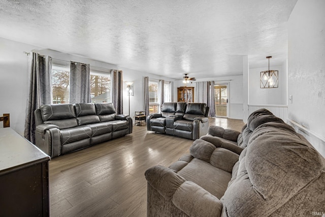 living room featuring hardwood / wood-style floors, ceiling fan with notable chandelier, and a textured ceiling