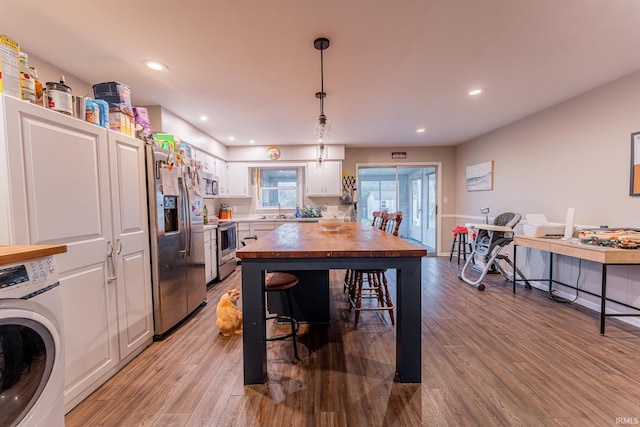 kitchen with white cabinetry, hanging light fixtures, hardwood / wood-style floors, washer / dryer, and appliances with stainless steel finishes