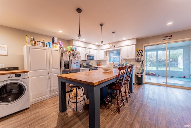 kitchen with appliances with stainless steel finishes, light hardwood / wood-style floors, pendant lighting, washer / clothes dryer, and white cabinetry