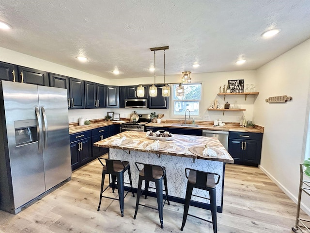 kitchen featuring sink, light hardwood / wood-style floors, decorative light fixtures, a breakfast bar area, and appliances with stainless steel finishes