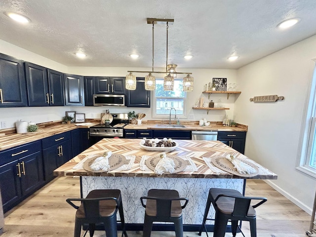 kitchen with appliances with stainless steel finishes, a breakfast bar, blue cabinets, sink, and a kitchen island