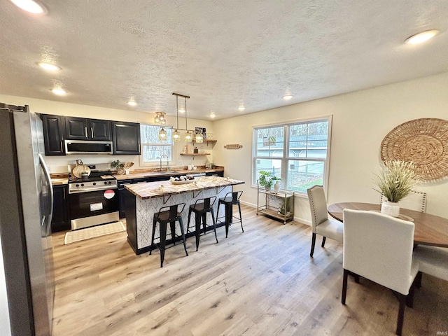 kitchen featuring appliances with stainless steel finishes, light wood-type flooring, a kitchen breakfast bar, pendant lighting, and a kitchen island