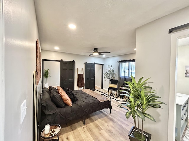 bedroom featuring a barn door, ceiling fan, and light hardwood / wood-style flooring