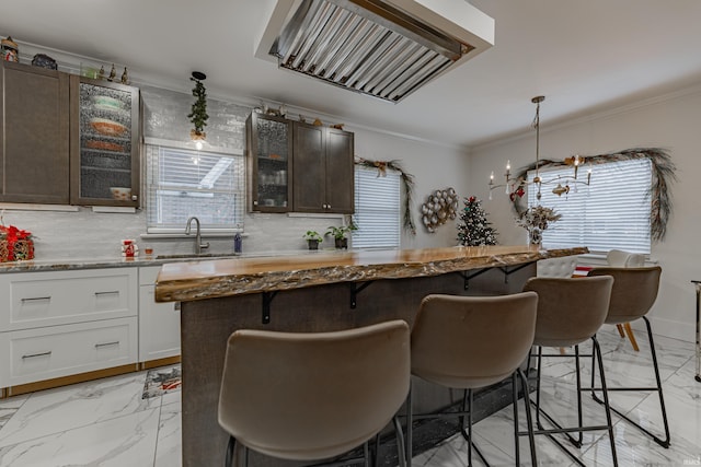 kitchen featuring a kitchen breakfast bar, dark brown cabinetry, sink, decorative light fixtures, and white cabinets