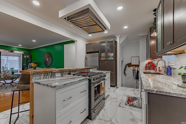 kitchen with a kitchen bar, ornamental molding, stainless steel appliances, sink, and white cabinetry