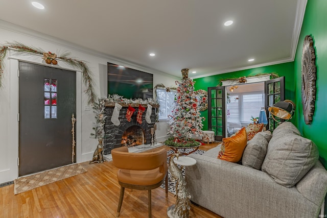 living room with a stone fireplace, wood-type flooring, and ornamental molding