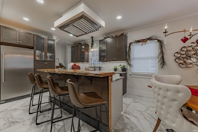 kitchen featuring sink, a kitchen island, high end fridge, dark brown cabinetry, and a breakfast bar area